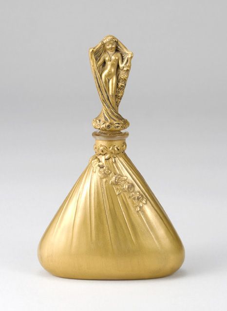 Perfume Bottle"Dalcrose"
England 1916. Dubarry perfume bottle. The stopper has a nude maiden wearing a veil that drapes down to “cover” the entire bottle. The highly elaborate design in a plated gold color indicates that the bottle once held an expensive perfume.