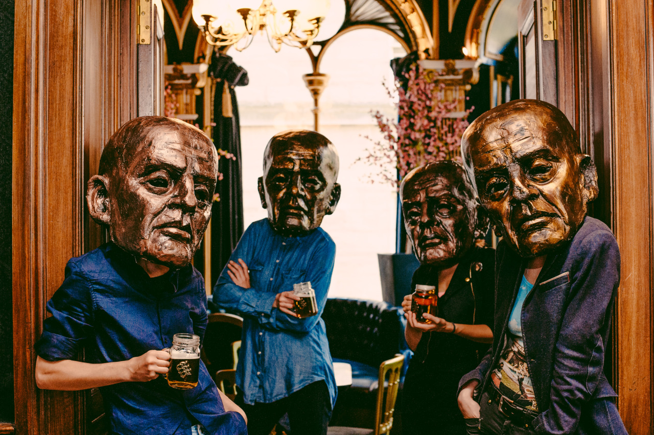 A picture of four people wearing large masks holding beer