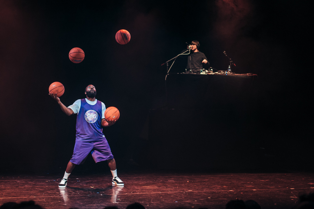 A man juggles four basketballs while another man djs