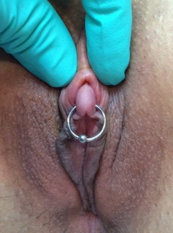 pussymodsgaloreA very nice clit, pierced and with a ring through it, the clit hood being retracted (by the gloved fingers of the piercer?).