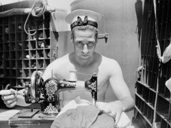 A Royal Navy sailor on board HMS Alcantara uses a portable sewing machine to repair a signal flag during a voyage to Sierra Leone, March 1942 - Cecil Beaton