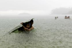 unrar:    A young girl covers herself from the rain with a banana leaf next to a man in the sea on the outskirts of Colon City, Carlos Jasso. 