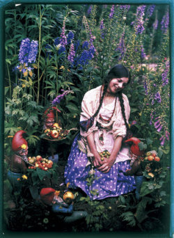 fawnvelveteen:Autochrome photograph by the well-known amateur photographer Mrs G A Barton, showing a young woman, Etheldreda Janet Laing (1872-1960), kneeling in a garden surrounded by flowers, fruit and garden gnomes