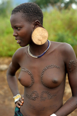 By Christophe Cerisier.  Mursi girl with large wooden earrings and body scarifications, Omo River Valley. Ethiopia 