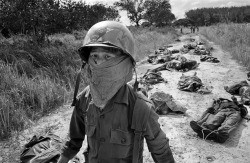 mortisia:  A Vietnamese litter bearer wears a face mask to keep out the smell as he passes the bodies of U.S. and Vietnamese soldiers killed in fighting against the Viet Cong at the Michelin rubber plantation, about 45 miles northeast of Saigon, Nov.