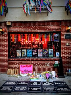 enoughtohold: memorial for the victims of the pulse shooting at the stonewall inn in nyc on the anniversary of the tragedy, featuring placards by laurie arbeiter and we will not be silent. a chalked rainbow in the center, identical to one chalked at the