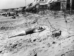 A woman sunbathes on a wartime bank holiday surrounded by barbed wire on the beach at Bournemouth, 1944.