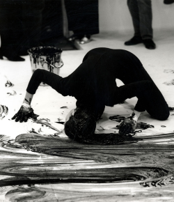 curties:  Janine Antoni in the documentation of the performance Loving Care. In it, Antoni uses her hair as a paintbrush and Loving Care hair dye as her paint. Antoni dips her hair in a bucket of hair dye and mops the gallery floor on her hands and