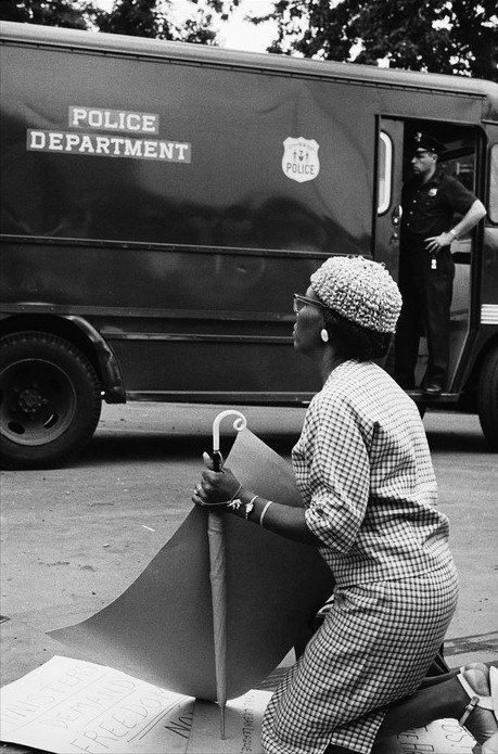A woman kneels in front of police at a civil rights protest, Brooklyn, 1963. Photographed by Leonard Freed.https://painted-face.com/