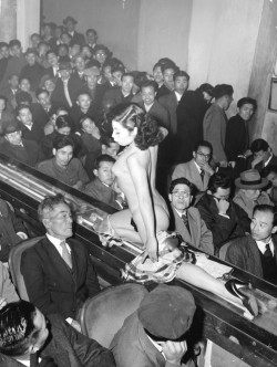 historicaltimes:  A stripper at a Tokyo striptease show is taken past the audience on a moving plastic conveyor belt, which is lit from underneath by neon lights, 1957 - 