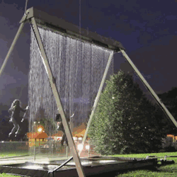 livetomakeadifference:   Towering steel swing set holding arrays of mechanical solenoids that create a water plane falling in the path of its riders. Riders pass through openings in a waterfall created by precisely monitoring their path via axel-housed