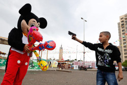 politics-war:  A Syrian refugee boy points a plastic toy pistol at a man in a Mickey Mouse costume in Beirut, Lebanon. Photograph: Jamal Saidi   Not a fan, obviously